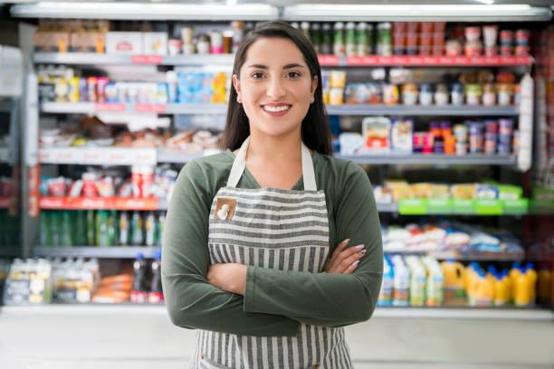 Young woman working at a market standing in front of the refrigerated section smiling at camera with arms crossed - Business industry concepts